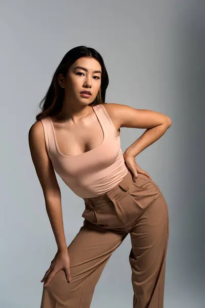 A young woman in a pink tank top and brown trousers stands confidently in a studio setting. — Stock Photo