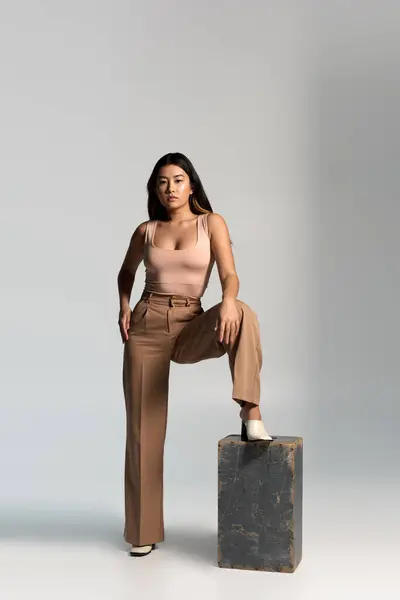 A young woman in stylish pants and a tank top poses with one foot resting on a block. — Stock Photo