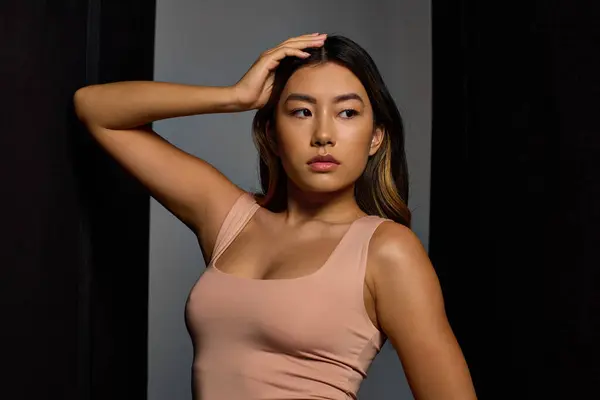 Una mujer en una camiseta rosa mira pensativamente mientras se toca el pelo. - foto de stock