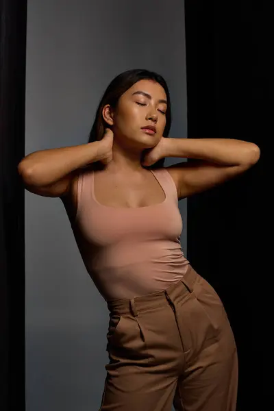 Young woman with dark hair strikes pose against backdrop, donning pink tank and brown pants. — Stock Photo