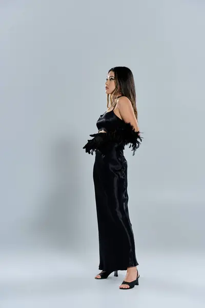 A stylish Asian woman stands in a black satin dress, looking away from the camera. — Stock Photo