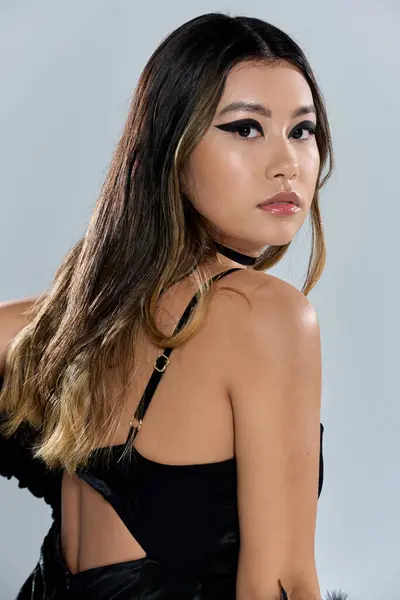 Eine Asiatin mit langen dunklen Haaren trägt ein stylisches schwarzes Kleid und blickt über ihre Schulter. — Stock Photo