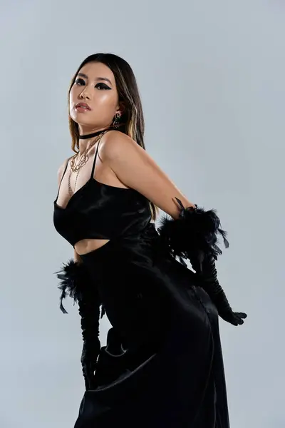 A woman in a black satin dress with feathered accents poses against a light gray backdrop. — Stock Photo