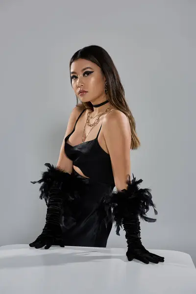 A woman wearing a black dress and feather gloves poses with her hands on a white table. — Stock Photo