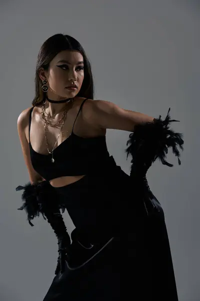 A woman in black, adorned with feathers, poses against a gray backdrop. — Stock Photo