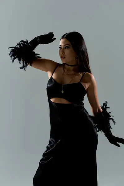 A woman in a black dress and feather gloves, gazing off-camera, with a backdrop of grey. — Stock Photo
