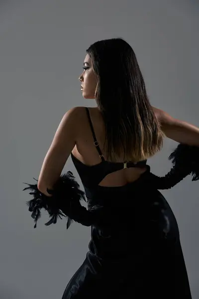 A woman in a black dress and gloves poses against a gray backdrop. — Stock Photo