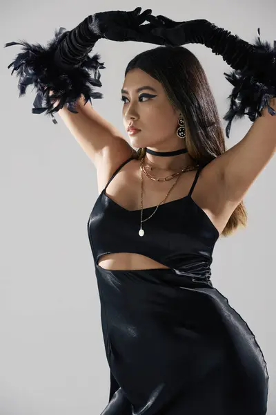 A woman in a black satin dress poses with feather gloves, her dark hair cascading down her back. — Stock Photo