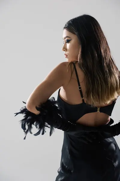 A woman in a black satin dress and feather embellishments poses against a white backdrop. — Stock Photo