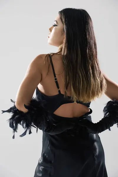 A woman in a black dress with feather accents stands with her back to the camera. — Stock Photo