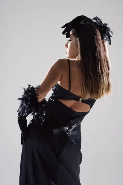 A woman in a black dress with feather accents poses against a simple background. — Stock Photo