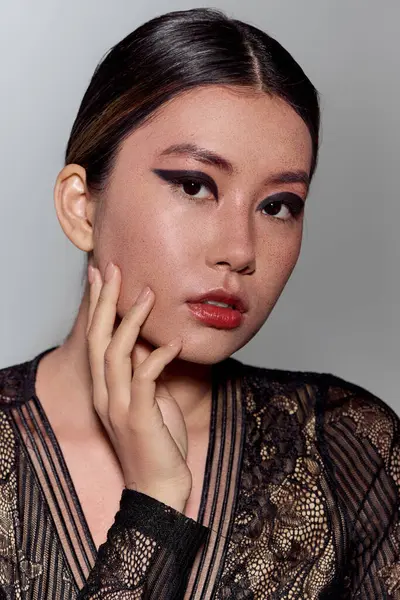 Eine schöne Asiatin posiert in einem schwarzen Spitzenkleid mit auffälligem Eyeliner. — Stockfoto