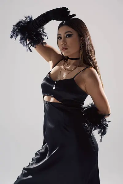 Asian woman in sleek black dress, poses confidently, adorned with a feather glove. — Stock Photo