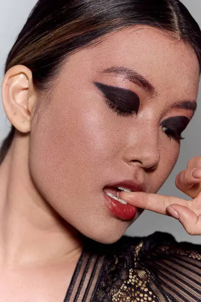Un primo piano di una donna asiatica con l'eyeliner scuro si morde il dito, fissando lateralmente. — Foto stock