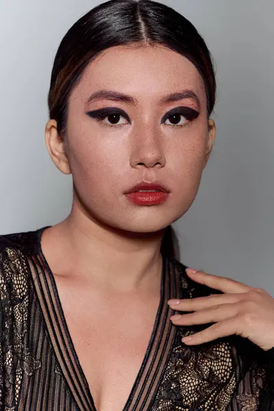 An Asian woman with dark eyeliner and red lipstick poses in a black lace top. — Stock Photo