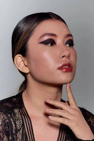 A young Asian woman with dark eyeliner and glossy lips poses for a studio portrait. — Stock Photo