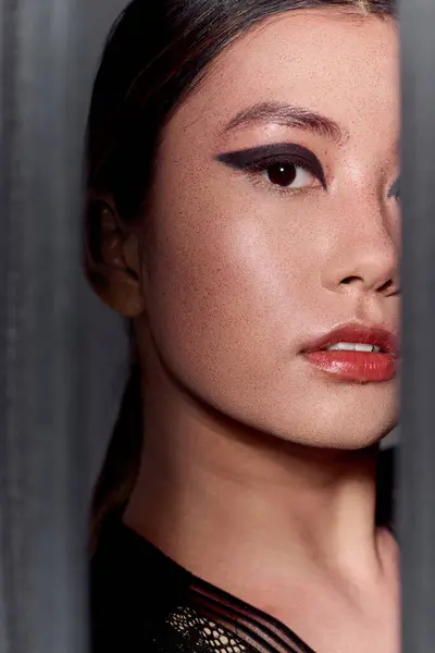 A woman with dark hair and dramatic eye makeup looks out from behind a textured wall. — Stock Photo
