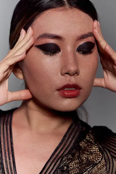 A young woman with dark eyeliner looks down, her hands gently touching her face. — Stock Photo