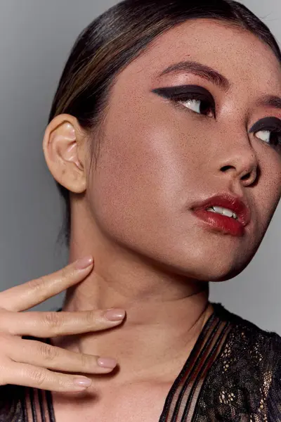 Un primo piano di una donna asiatica con eyeliner scuro, con un top di pizzo nero, che guarda lateralmente. — Foto stock