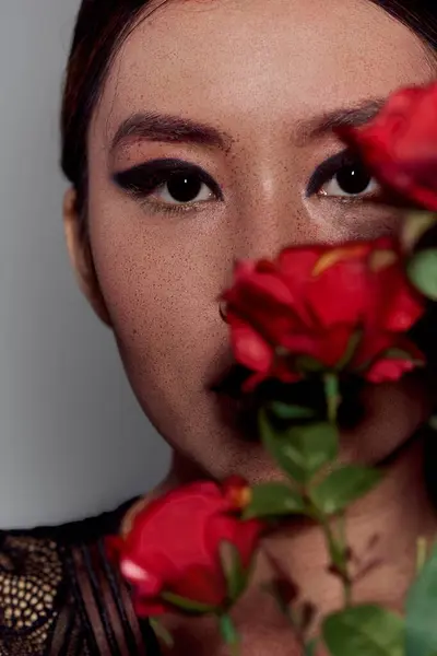 An Asian woman with bold makeup gazes into the camera, a rose obscuring her mouth. — Stock Photo