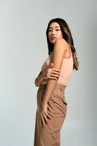 Asian woman in pink tank top and brown pants poses against white background. — Stock Photo