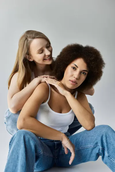 A lesbian couple in white tank tops and jeans pose on a grey background. — Stock Photo