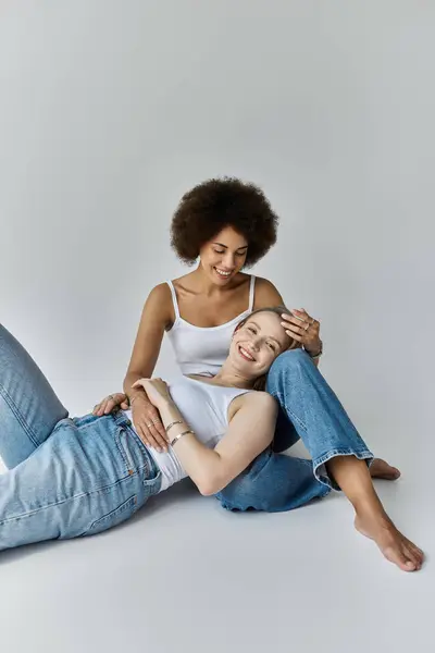 A lesbian couple, share a tender moment while dressed in casual attire, against a simple grey backdrop. — Stock Photo