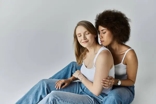 Two women, one with blonde hair and one with dark curly hair, sit close to each other and embrace in a studio setting. — Stock Photo