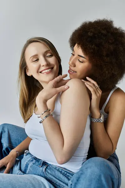A lesbian couple, one with long blonde hair and the other with an afro, share a tender moment, both wearing white tank tops and jeans. — Stock Photo