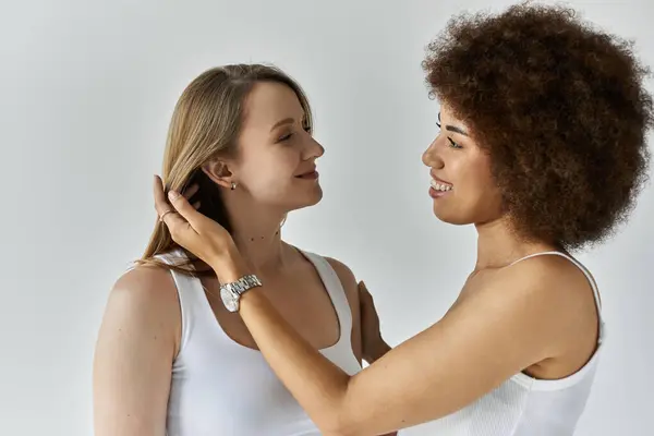 Two women in white tops and jeans stand close, gazing affectionately at each other against a grey background — Stock Photo