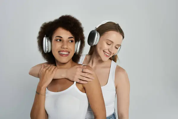 Duas mulheres no topo do tanque abraçam enquanto ouvem música com fones de ouvido. — Fotografia de Stock