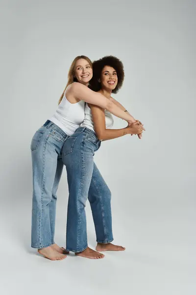 Two women in tank tops and jeans smile as they pose for the camera, with the woman on the left arm around the woman on the right — Stock Photo