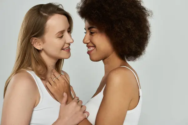 Dos mujeres, una con el pelo largo y rubio y la otra con rizos, miran amorosamente a los ojos, sus manos entrelazadas. - foto de stock