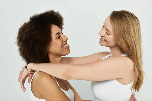 Two women, one with afro hair and the other with long blonde hair, embrace and smile at each other. — Stock Photo