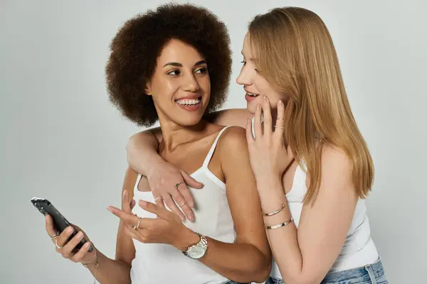 Zwei Frauen in weißen Tank-Tops lächeln und schauen einander an, während sie ein Telefon in der Hand halten. — Stockfoto