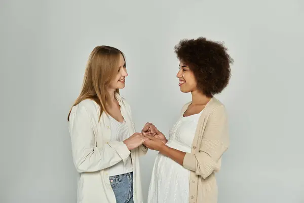 Dos mujeres, una embarazada, cogidas de la mano y mirándose con una sonrisa. — Stock Photo