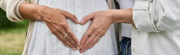 A pregnant Black woman and her partner stand outdoors, their hands forming a heart shape on her belly. — Stock Photo