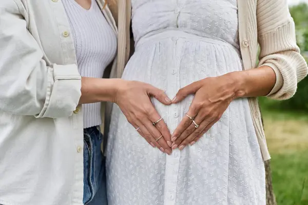 A pregnant woman with her partner, their hands forming a heart shape over the belly. — Stock Photo