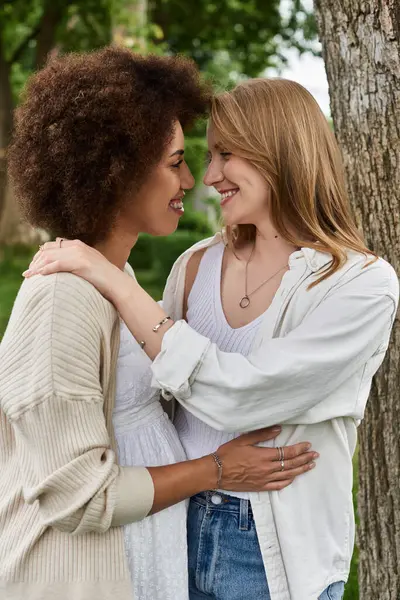 Two women embrace, one pregnant, as they stand in a park. — Stock Photo