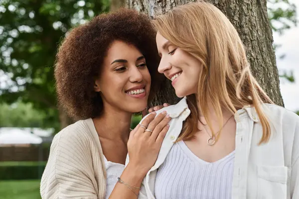 Two women, lovingly gaze at each other while standing near a tree. — Stock Photo