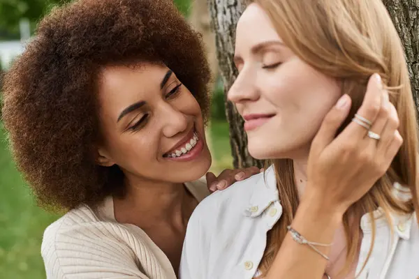 Eine Afroamerikanerin und ihr lesbischer Partner stehen gemeinsam an einem Baum und umarmen sich liebevoll. — Stockfoto