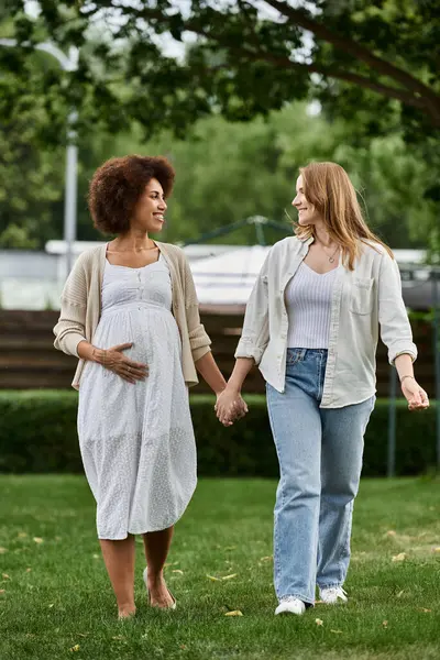 A pregnant Black woman and her partner walk hand-in-hand in a park, smiling and looking at each other. — Stock Photo