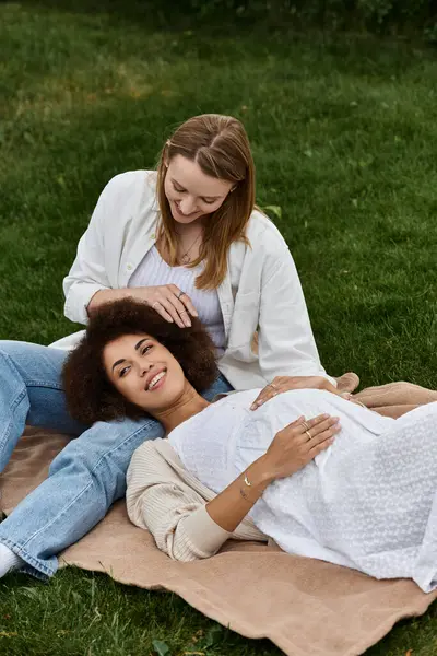 A pregnant woman rests on the lap of her partner while they relax on a blanket in a grassy park. — Stock Photo