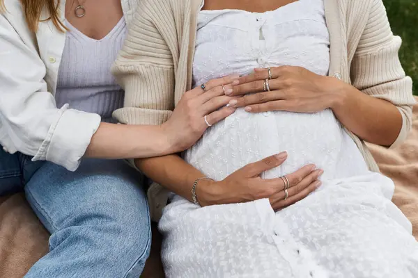 Una mujer afroamericana embarazada se sienta junto a su pareja, sosteniendo a un bebé en sus brazos. - foto de stock