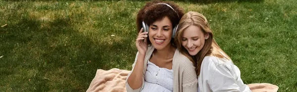 Happy African American woman and her partner relax on a blanket in a grassy park while listening to music. — Stock Photo