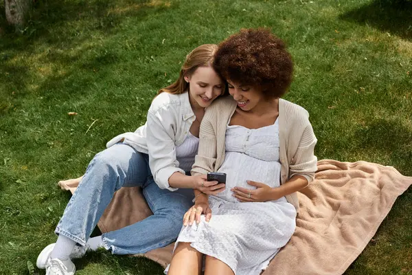 A pregnant woman with a large belly rests her hand on her stomach while her partner looks at a phone. — Stock Photo