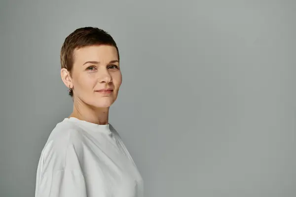 A woman with short hair standing against a grey background, confidently looks towards the camera. — Stock Photo