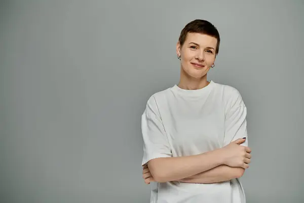 Коротковолосая женщина уверенно улыбается, скрещенные руки, в белой футболке, осознание рака груди — стоковое фото