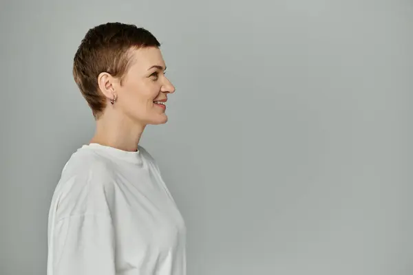 Короткошерста жінка в білій футболці посміхається, стикаючись в бік, обізнаність про рак молочної залози — стокове фото