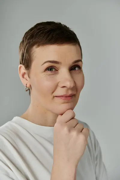 A woman with short hair, signifying breast cancer awareness, poses against a grey background. — Stock Photo